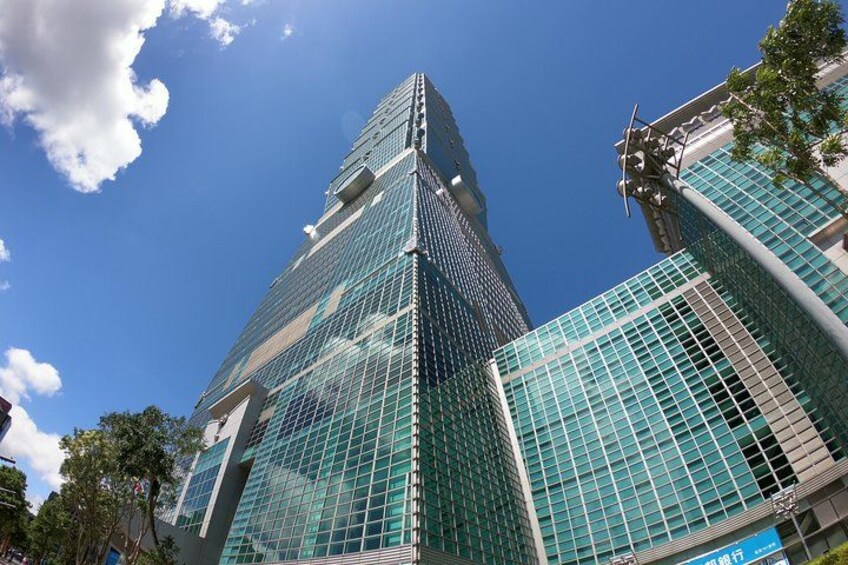 Un rascacielos alto de vidrio con diseño moderno, rodeado de otros edificios y árboles. 3