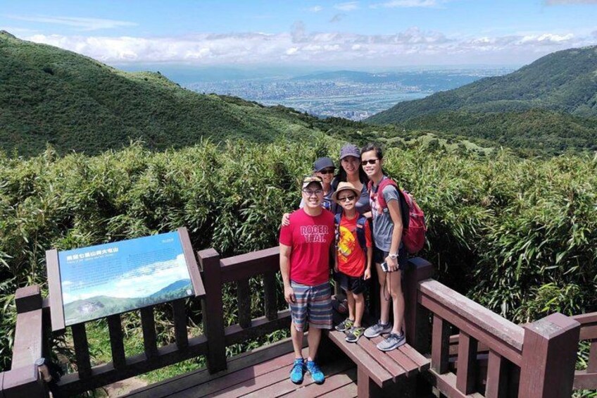 Un grupo de personas sobre una plataforma de madera con vistas panorámicas a colinas y una ciudad distante. 4