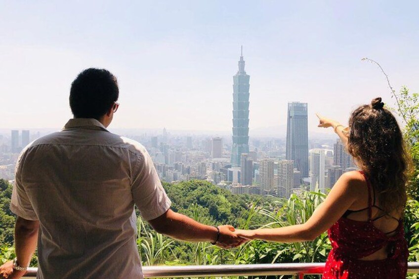 Una pareja tomándose de las manos contemplando un paisaje urbano con una torre destacada. 2