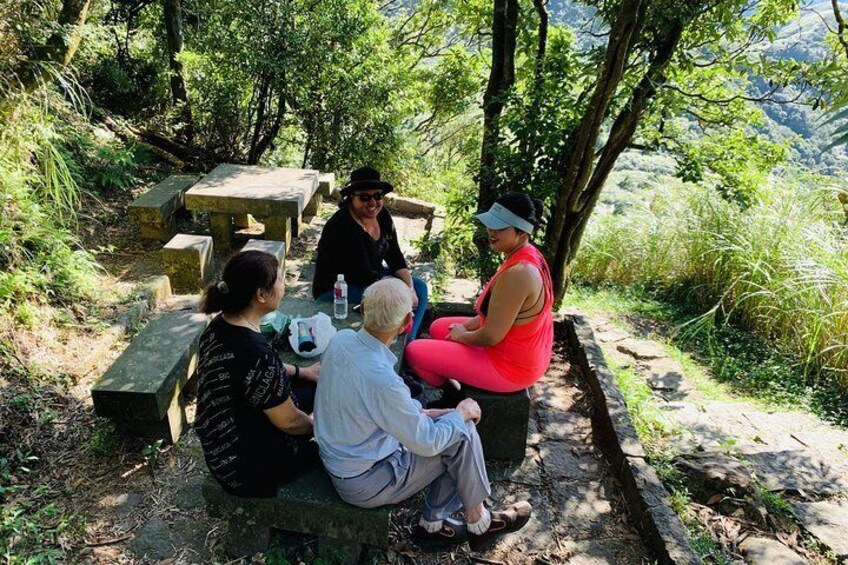 Four people sitting at a picnic table in a wooded area with a stone bench and a stone wall. 5