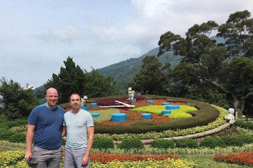 To personer står i en have med farverige blomster og statuer. 2