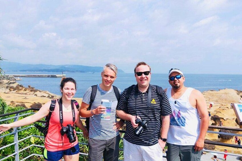 A group of people standing on a coastal overlook with a view of the sea and distant mountains. 2