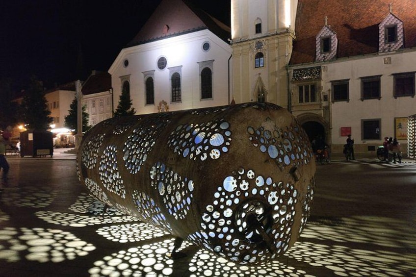 A large, illuminated sculpture with circular patterns, set against a backdrop of buildings and a night sky. 4