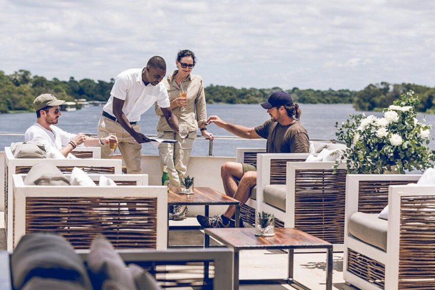 A group of people on a boat with outdoor seating, a lake, and greenery in the background. 2