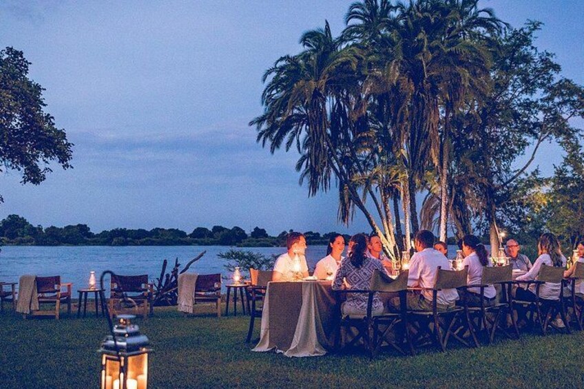 An outdoor dining area with tables and chairs, palm trees, and a body of water in the background. 1