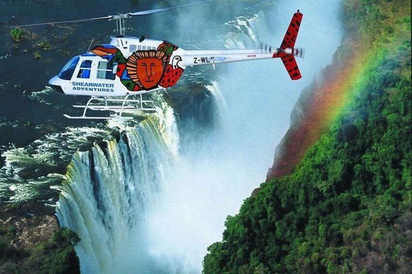 A helicopter flying over a waterfall with a rainbow. 2