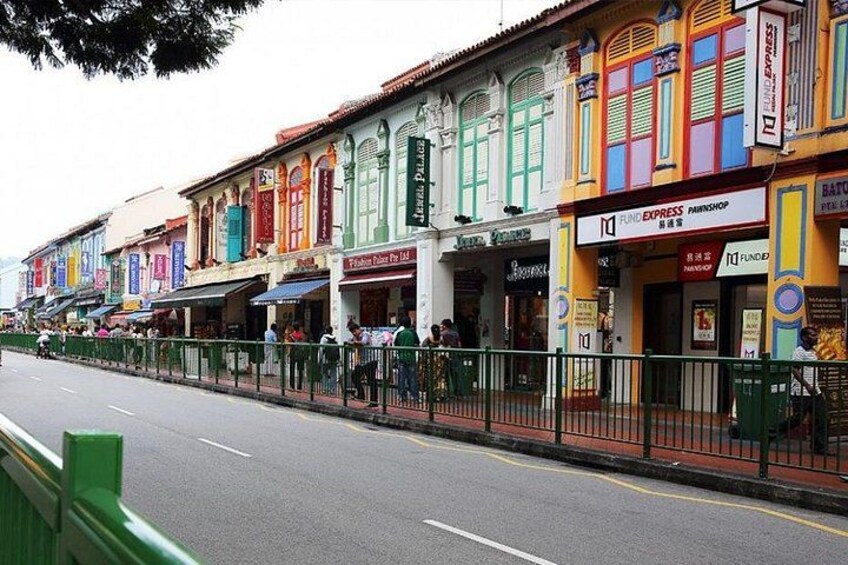 Una calle bordeada de edificios coloridos, una valla verde y una carretera con línea blanca. 2