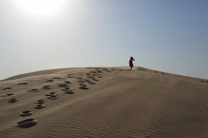 Une personne marchant sur une dune de sable, avec des empreintes de pas qui mènent jusqu'à elle. 5