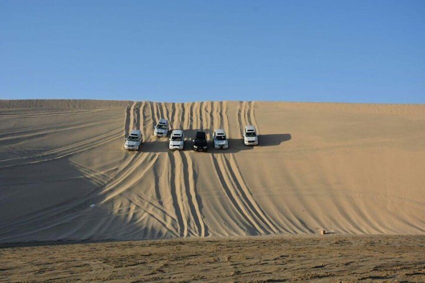 Un paysage désertique avec un groupe de véhicules stationnés sur une dune de sable. 3