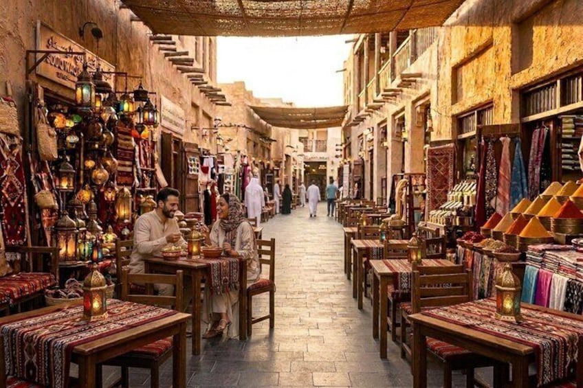 A narrow street with shops on either side, tables and chairs outside, and people walking in the distance. 1