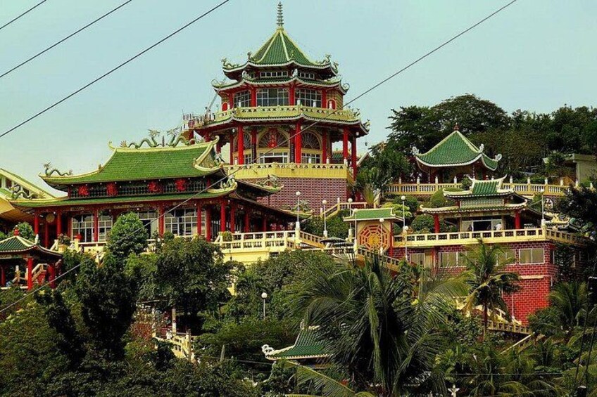 Een traditionele, meerlaagse pagode met groene daken, omgeven door weelderig groen en palmbomen. 3