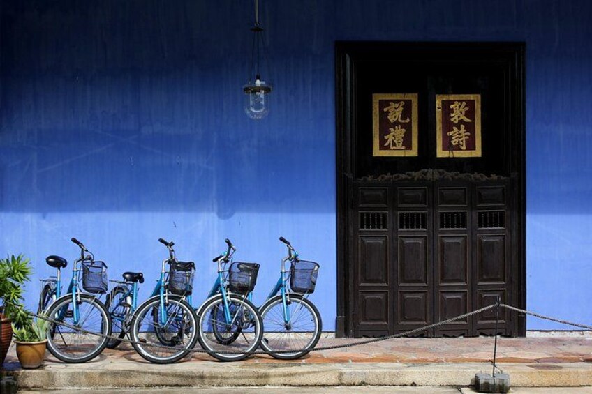 A row of bicycles parked in front of a building with a blue wall and a dark brown door. 4