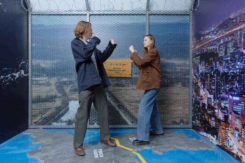 Two people in a room with a cityscape mural, a sign with text, and a map on the floor. 3