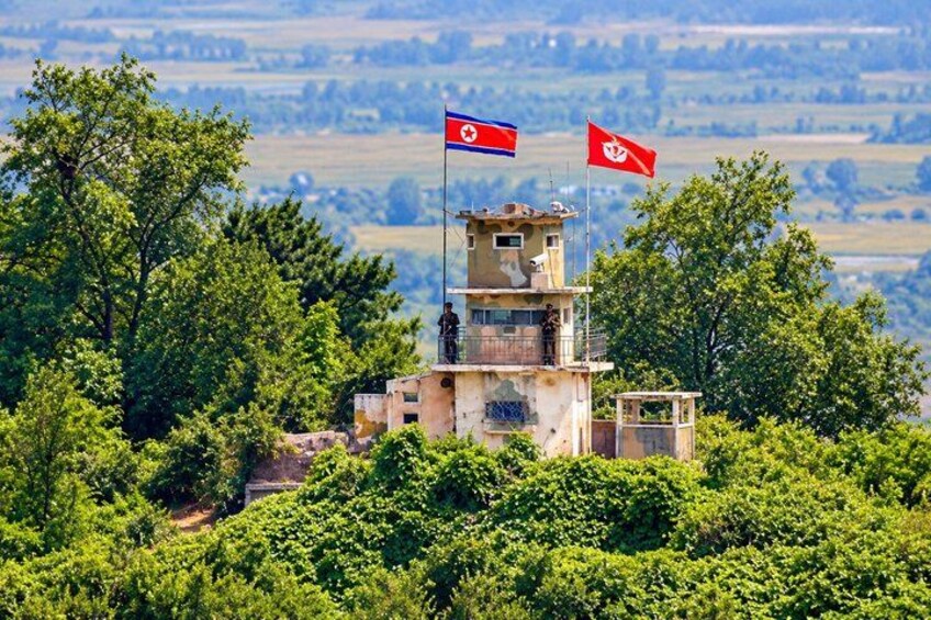 A watchtower with two flags, surrounded by lush greenery and hills in the background. 4