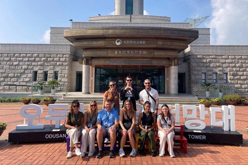 A group of people posing in front of a building with a large sign that reads 'ODUSAN TOWER'. 2