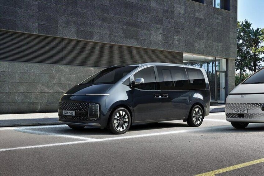 Una minivan oscura estacionada en una calle, con un edificio moderno al fondo. 3