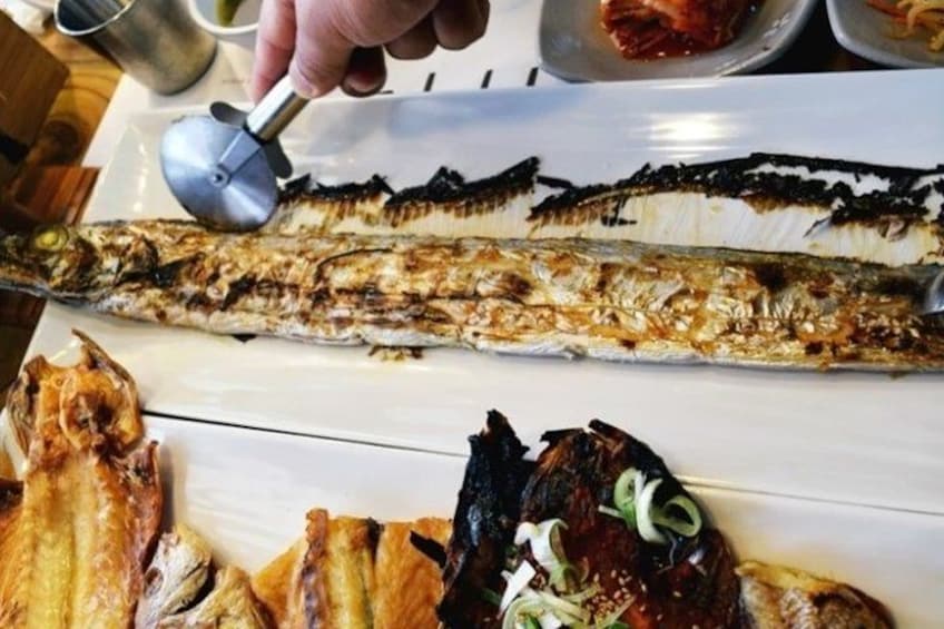 A grilled fish being sliced with a metal tool. 2