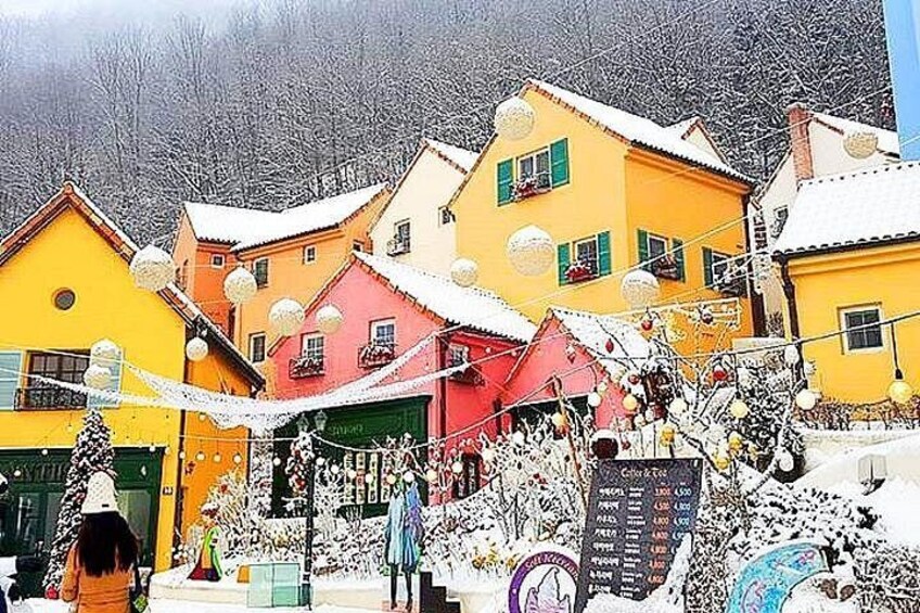 A snowy village with colorful houses, a person in winter clothing, and a signboard. 1