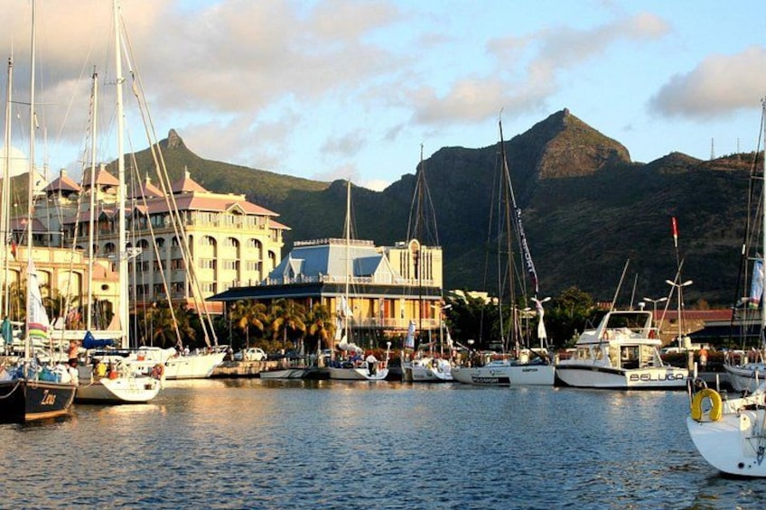 A marina with several sailboats docked, a building with a red roof, and mountains in the background. 1