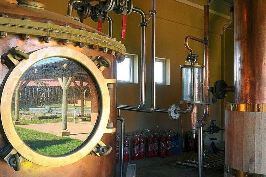 A distillery with copper pipes, a large circular window, and a view of a park. 3