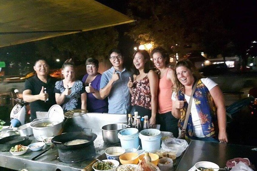 A group of people standing around a table with cooking equipment and food items. 2