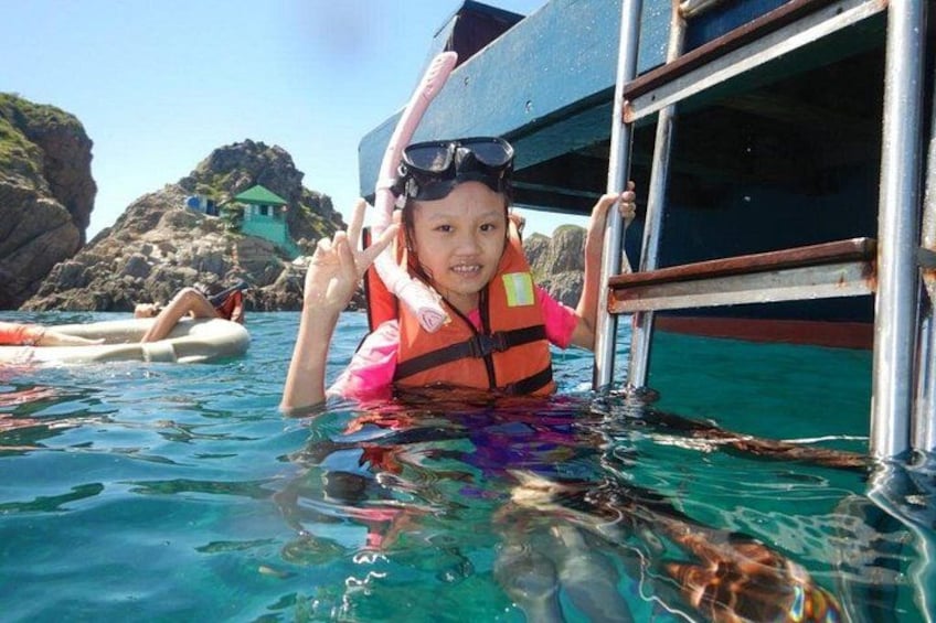 A person in a life jacket and snorkel gear in clear water, with a boat and rocky landscape in the background. 4