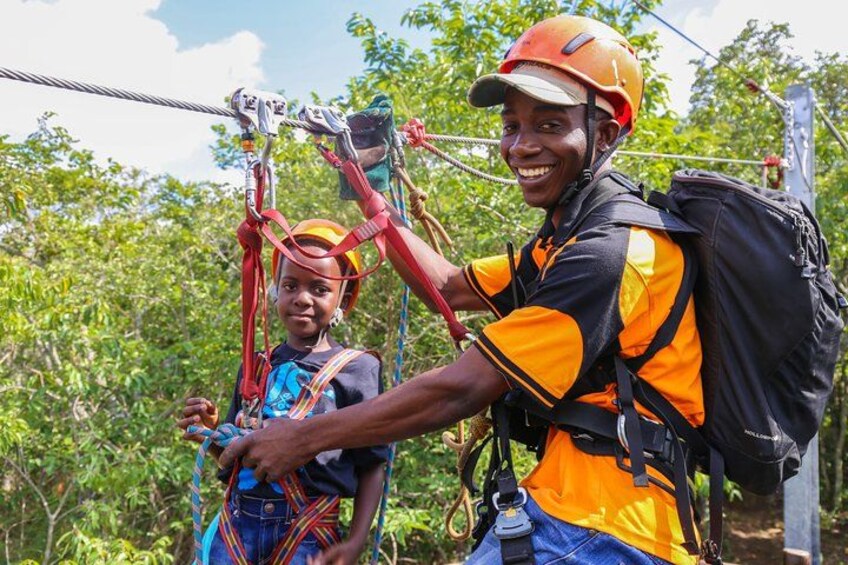 Two people wearing helmets and harnesses, preparing for a zip-lining activity in a forested area. 2