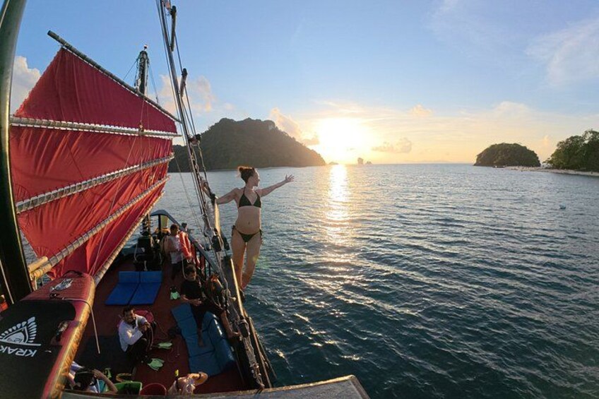 Una persona su una barca con una vela rossa, un tramonto sullo sfondo e un mare calmo. 2