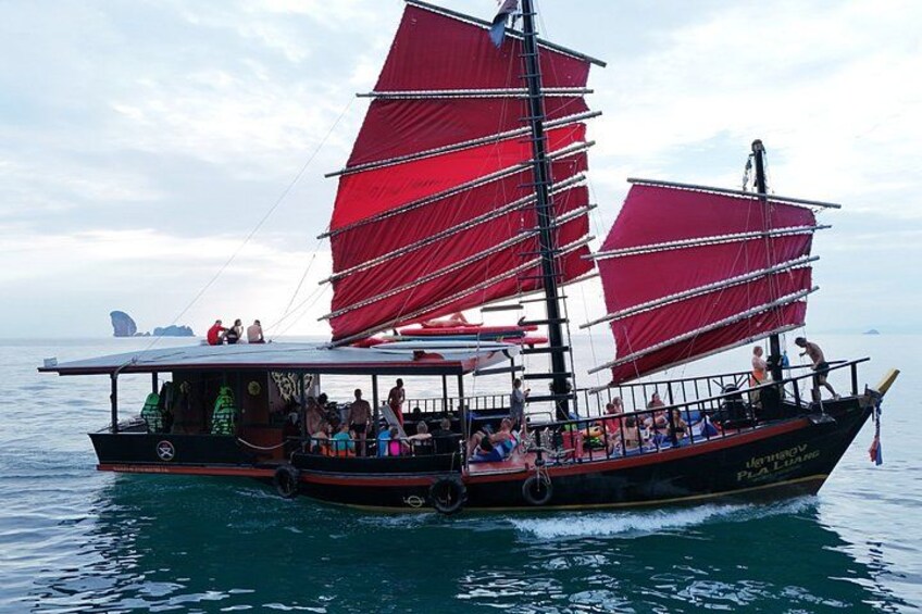 Una tradizionale barca a vela con vele rosse, passeggeri e una vista ampia sull'oceano. 1