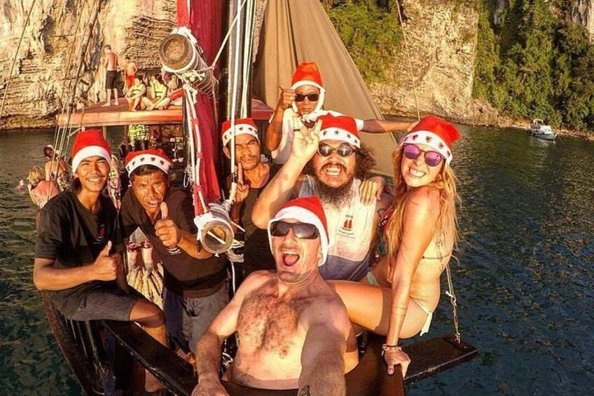 Un gruppo di persone su una barca che indossano cappelli da Babbo Natale, con una scogliera rocciosa e acqua sullo sfondo. 5