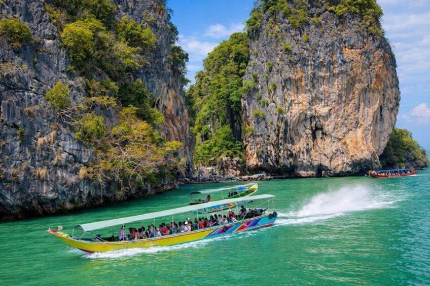 A boat tour with passengers, surrounded by rocky cliffs and clear turquoise water. 2