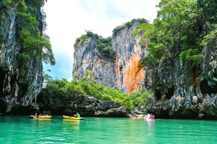 A kayaker in a turquoise sea, surrounded by rocky cliffs and lush greenery. 3