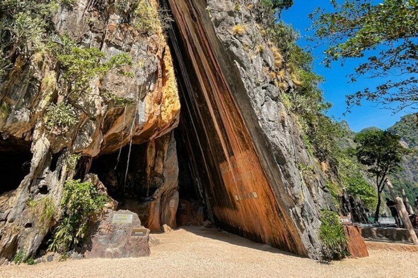 A large rock formation with a cave entrance, surrounded by greenery and a clear sky. 2