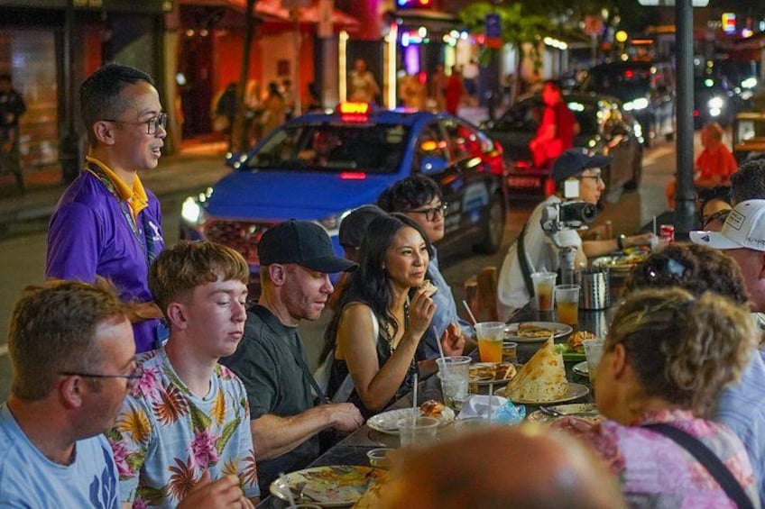 A group of people dining outdoors at night with cars and street lights in the background. 5