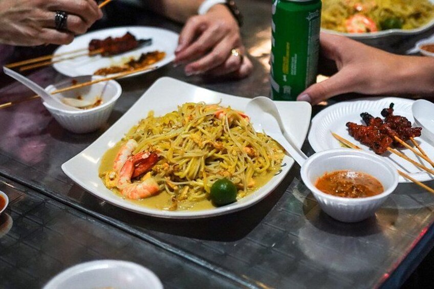 A table with various dishes, including noodles with shrimp, a plate of meat, and a bowl of sauce. 3
