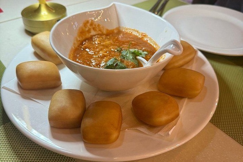 A white bowl of soup with a spoon, surrounded by six small, round, golden-brown items on a white plate. 5