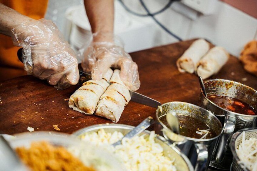 Eine Person bereitet Essen zu, insbesondere rollt sie ein Gericht, wobei verschiedene Zutaten und Utensilien sichtbar sind. 3