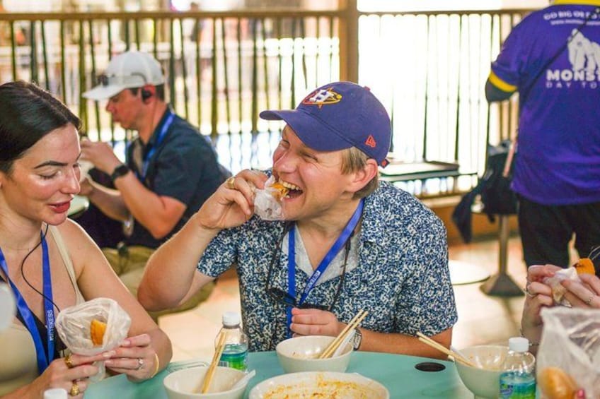 Menschen sitzen an einem Tisch mit Essen und Getränken, sie tragen Ausweise um den Hals. 3