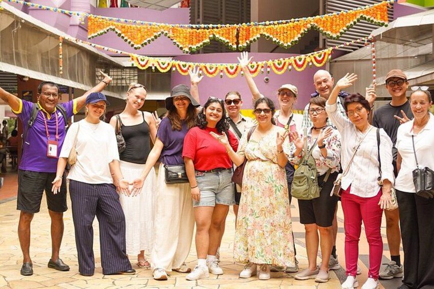 A group of people posing for a photo in an outdoor setting with a purple building and decorative garlands in the background. 4