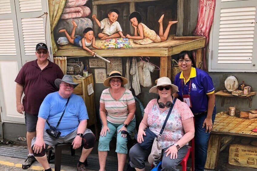 A group of people posing in front of a shop with a painting and various items on display. 1