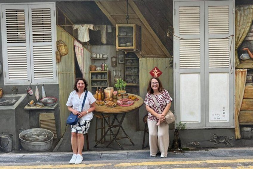 Two people standing in front of a traditional shop with wooden shutters and a variety of goods displayed outside. 4