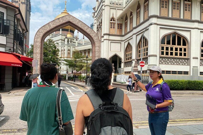 A street scene with a large archway, a building with ornate architecture, and people walking. 5