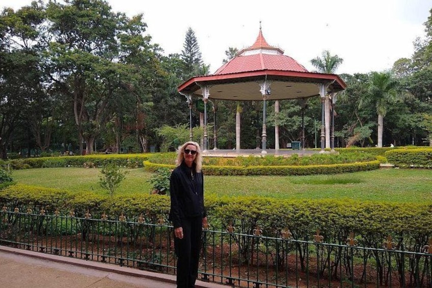A person standing in front of a gazebo in a park with manicured bushes and trees. 1