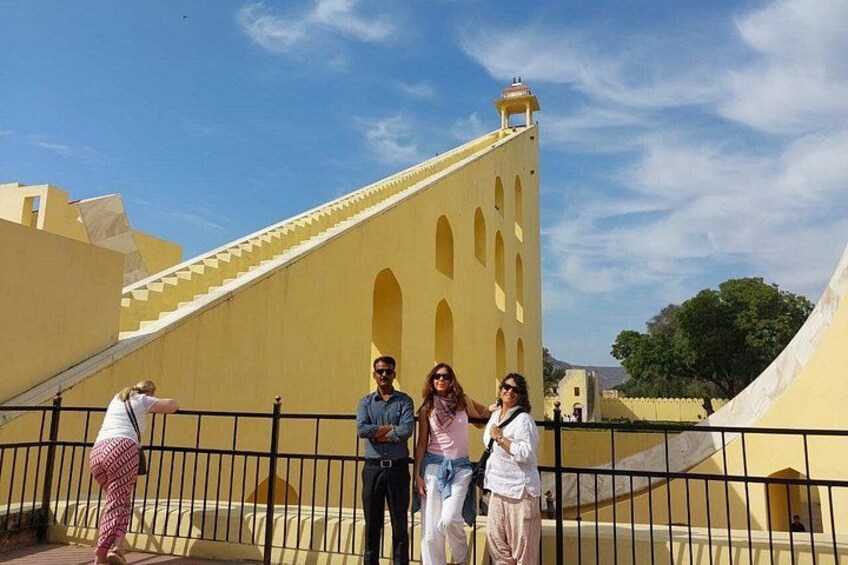 A group of people standing in front of a yellow building with a staircase and a tower. 3