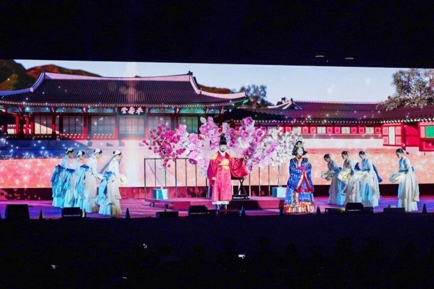 A stage with performers in traditional costumes, a backdrop of a traditional building, and cherry blossoms. 1