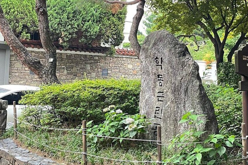 A large stone monument with Korean inscriptions, surrounded by greenery and a stone wall. 3