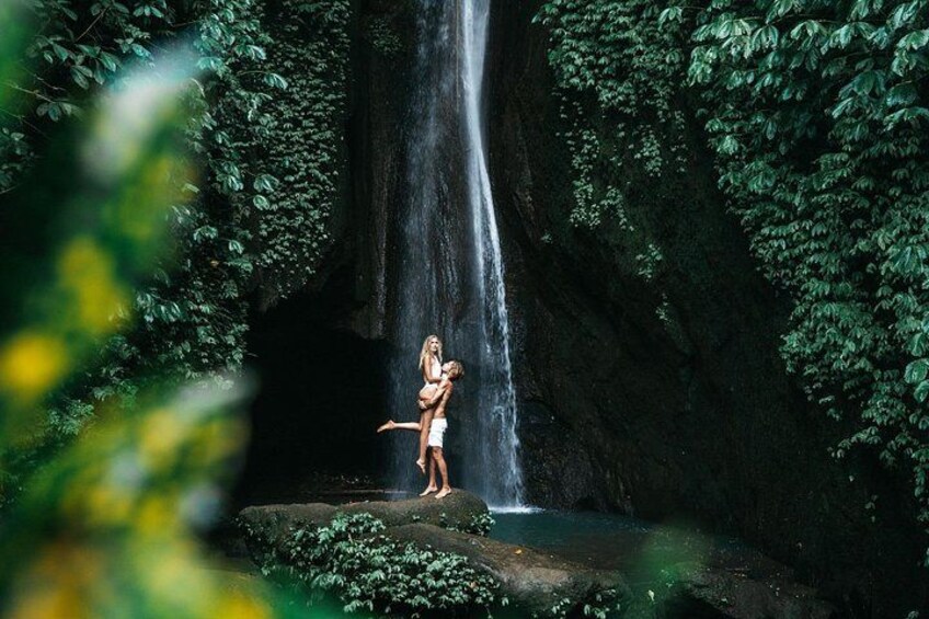 A waterfall, lush greenery, and a person standing on a rock. 4