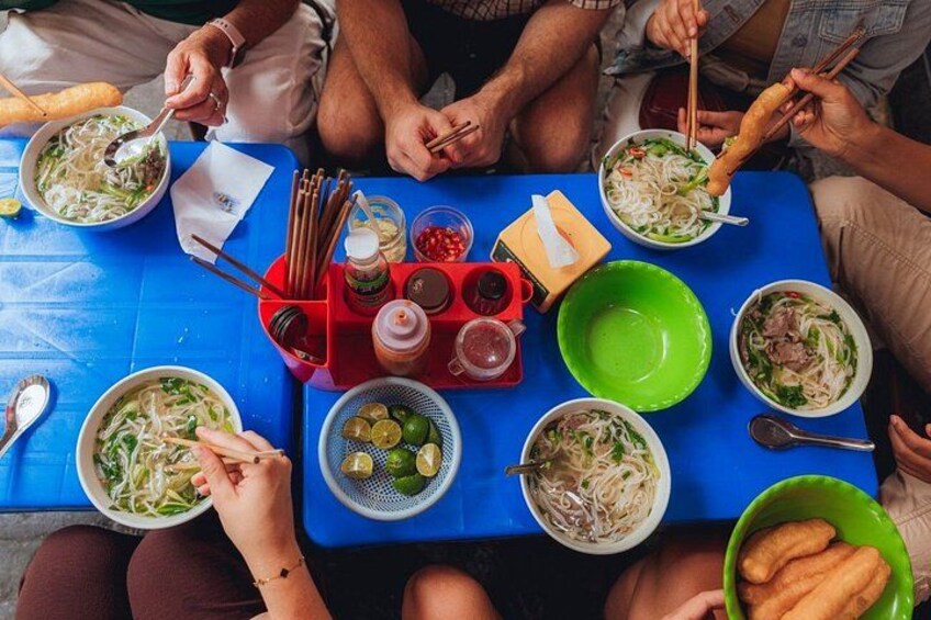 Un grupo de personas sentadas alrededor de una mesa con diferentes fuentes de comida, palillos y salsas. 4