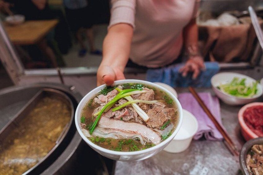 A person holding a bowl of soup with meat and green onions. 2