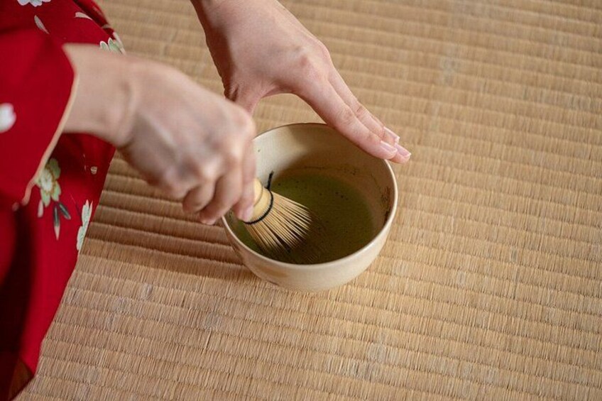 Eine Person schlägt Matcha in einer Schale auf einer Tatami-Matte auf. 3